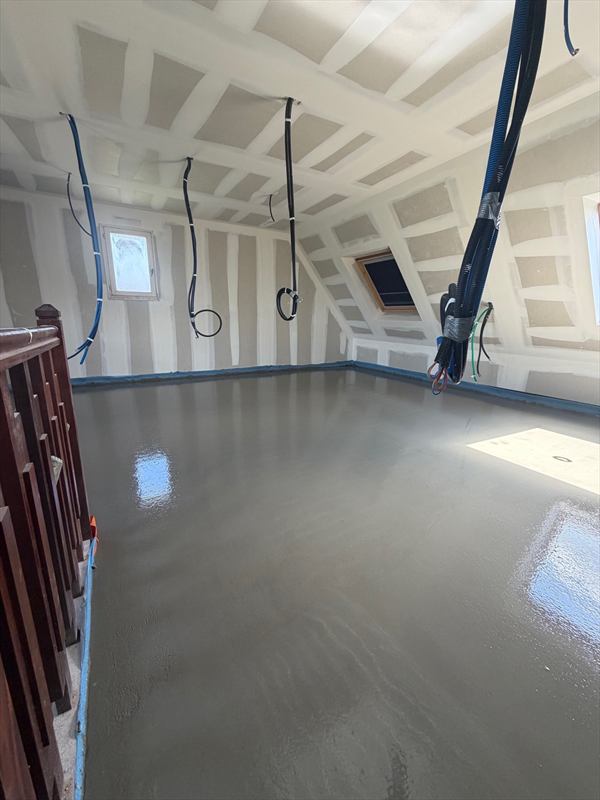 Chape liquide grise et lisse dans un comble aménagé, le long d'une rampe d'escalier en bois